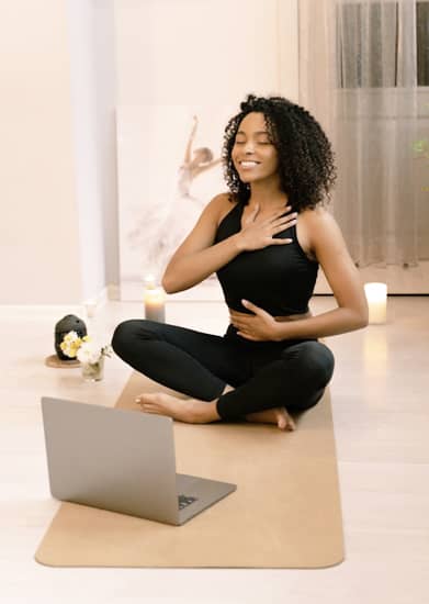 Photo d'une femme souriante sur un tapis de yoga dans la posture du lotus de yoga, devant elle un ordinateur portable